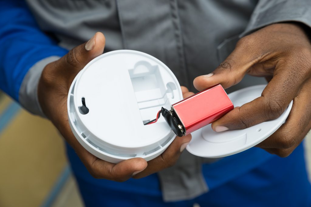 A homeowner changes the battery in a fire alarm