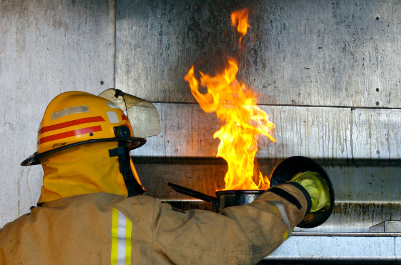 A firefighter demonstrates how to put out a gas fire with a heavy metal lid